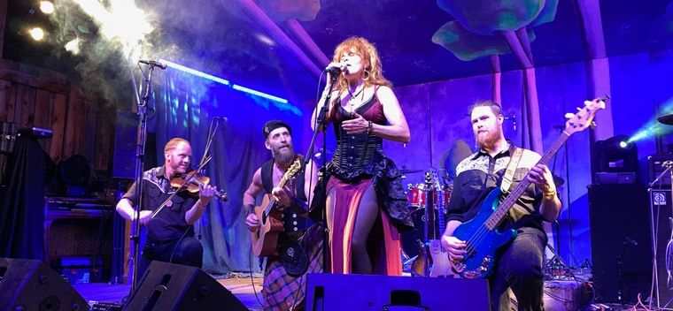 Dream Heavy on a festival stage, a singer at the microphone with a fiddler, guitarist and bassist behind her under purple light