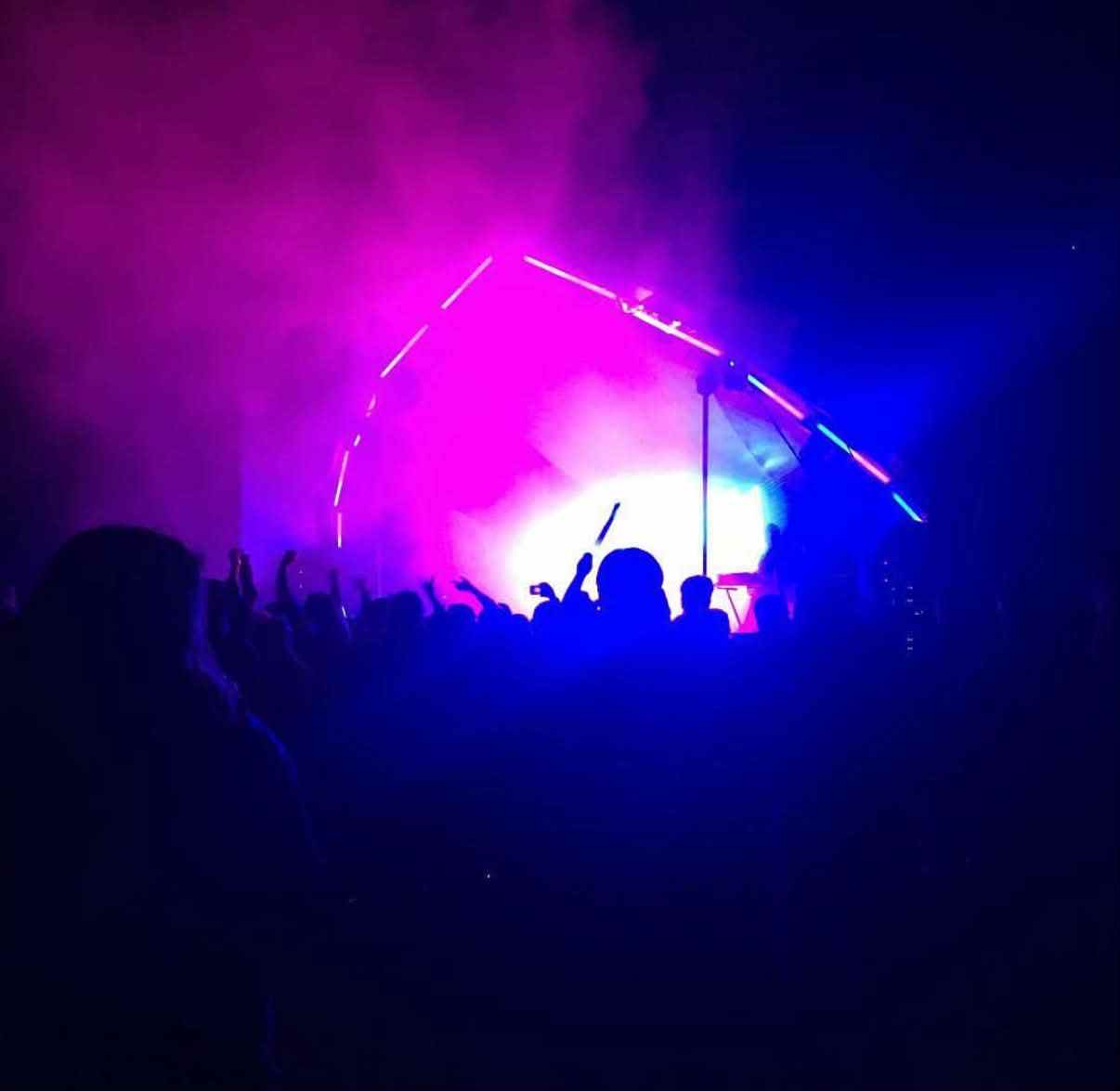 A crowd in front of a stage lit magenta and blue